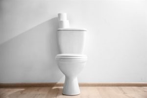 A white toilet with white toilet paper rolls against a white wall background