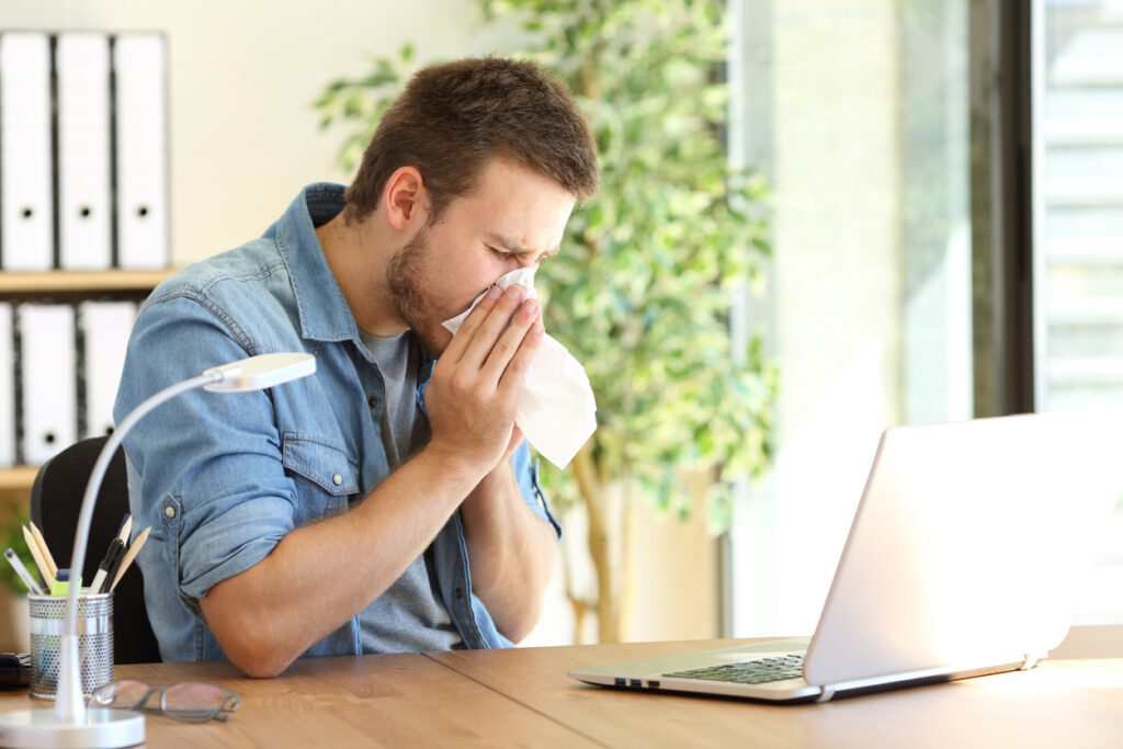 sneezing man with a tissue in office near a window